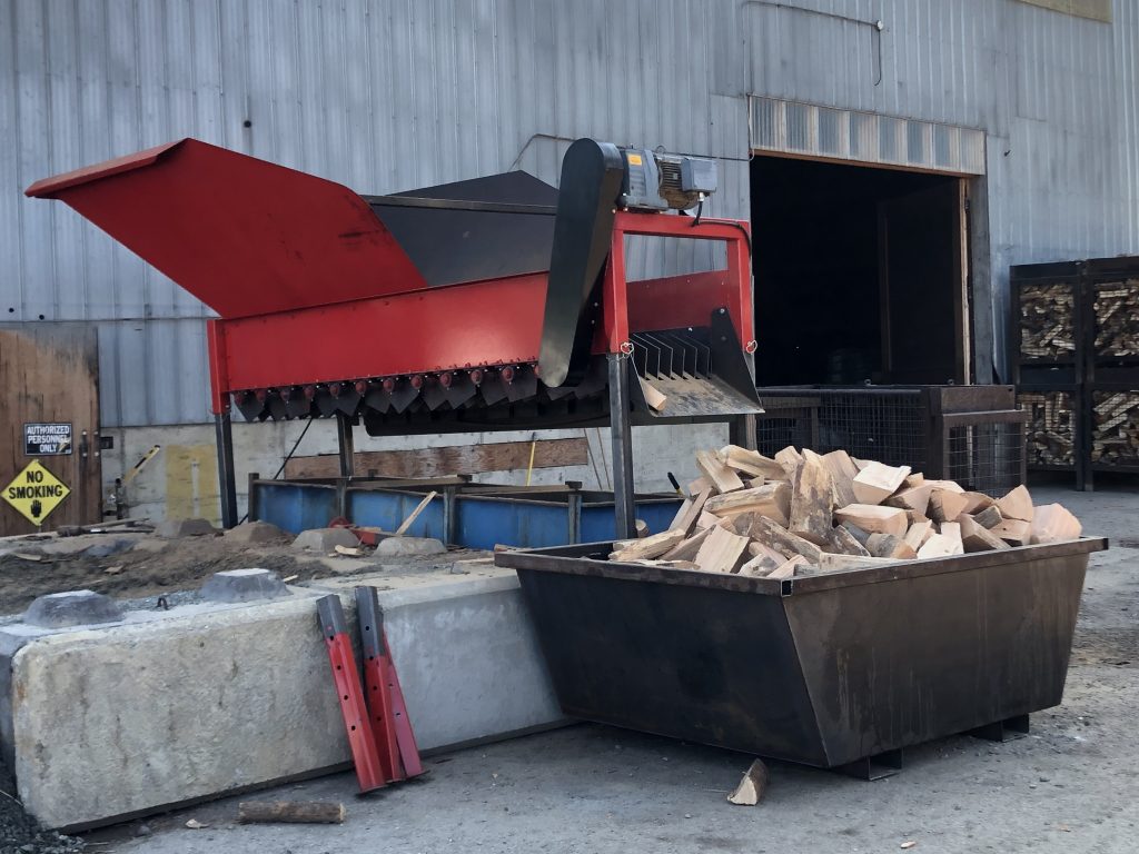An industrial wood chopper, made of red and grey sheet metal.