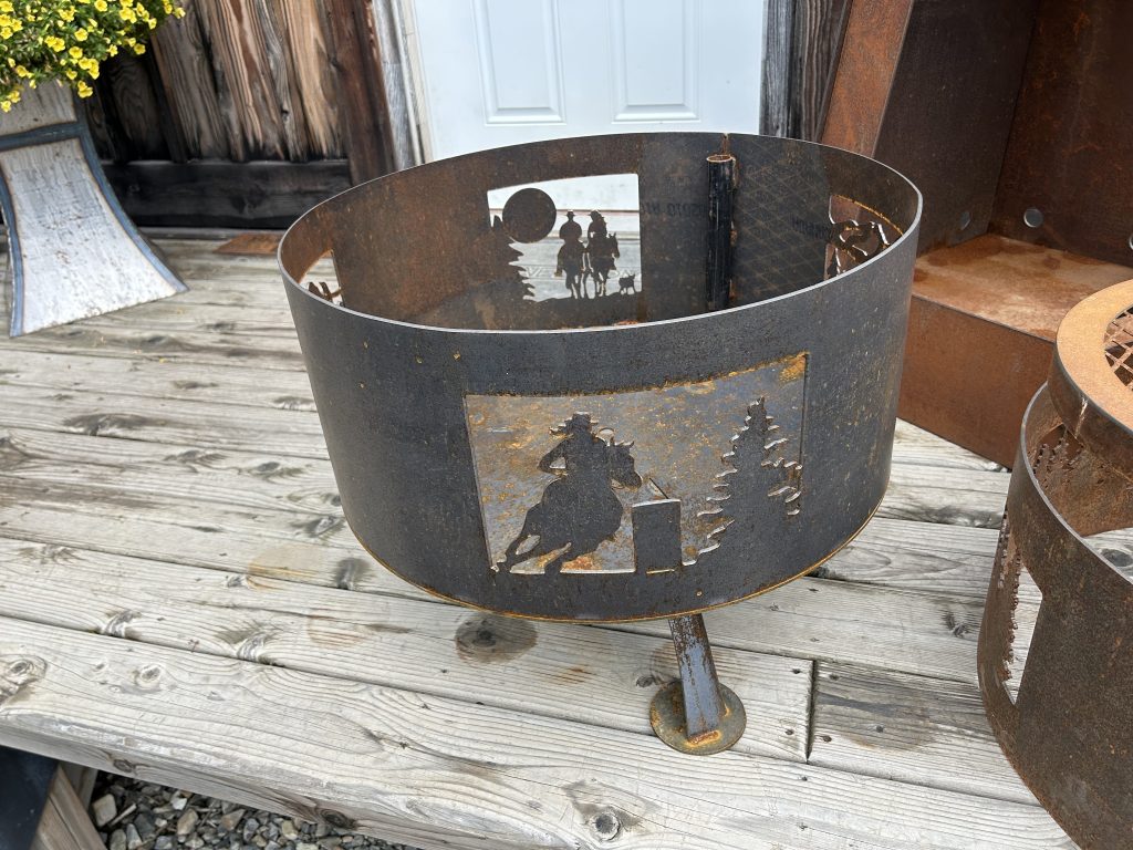 A metal circular firepit guard with depictions of cowboys riding horses etched out of the metalwork.