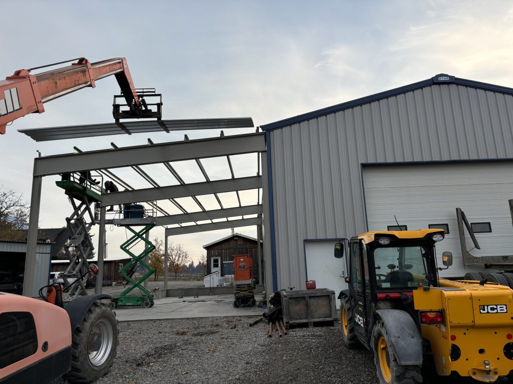 A construction site with machinery and workers putting together a metal roof.